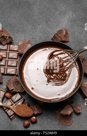 ceramic bowl of chocolate cream or melted chocolate and pieces of chocolate on dark concrete background Stock Photo