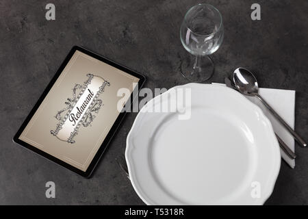 Tablet with stylish restaurant logo and laid table  Stock Photo