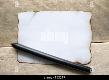 On wooden boards, there is a black pen, a white sheet of paper burnt at the edges, leaving room for text. Concept background. Stock Photo
