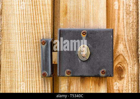 A weathered and worn metal lock mechanism with rusted screws on a wooden gate and fence post close up Stock Photo