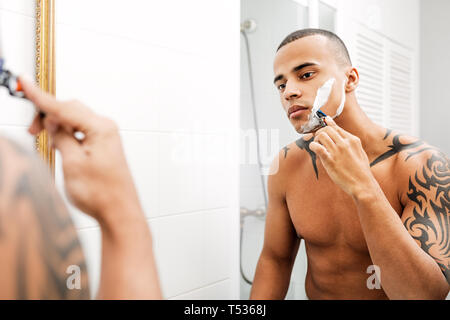 Portrait of a handsome young man shaving his facial hair in the bathroom Stock Photo