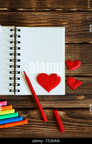 Blank notepad with felt-tip pens and red hearts on wooden background. Preparation for congratulations on Valentine's Day. Template. Vertical image. Stock Photo
