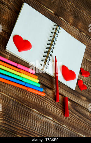 Blank notepad with red hearts and multi-colored felt-tip pens on a wooden background. Preparation for congratulations on Valentine's Day. Template. Ve Stock Photo