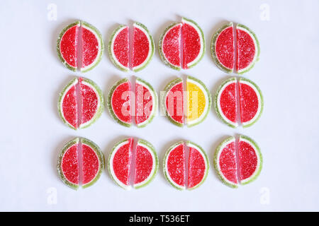 Marmalade in the form of slices of watermelon and lime on a white surface. Stand out from the crowd: one yellow and many red Stock Photo
