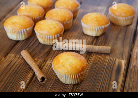 Cinnamon sticks and fresh golden muffins lie on the wooden surface of pine planks. Tasty and healthy food. Daylight. Stock Photo