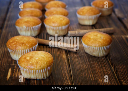 Fresh golden muffins and cinnamon sticks lie on a wooden surface made of pine boards. Tasty and healthy food. Daylight. Stock Photo
