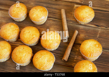 Cinnamon sticks and golden cupcakes lie on the wooden surface of pine planks. Tasty and healthy food. Daylight. Stock Photo