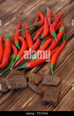 Red chili peppers and crackers of black bread with garlic lie on a wooden rustic table made of pine boards. Daylight. Vertical picture Stock Photo