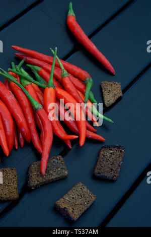 Brown spiced rusks and red chilli pods lie on a black wooden rustic table. Daylight. The surface of painted pine boards. Vertical image. Stock Photo