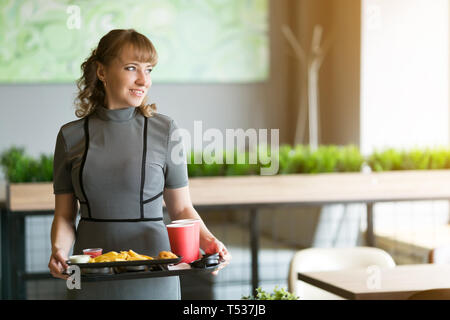 A woman of 30-35 years old is holding in her hands a dressing on   which juice is water food sushi rolls french fries. Stock Photo