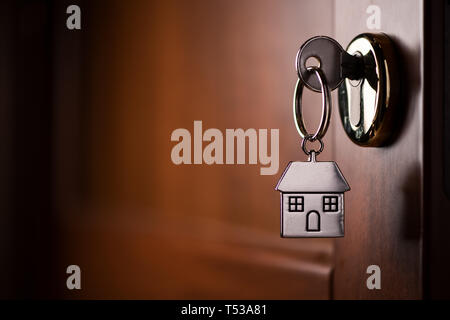House key on a house shaped silver keyring in the lock of a door Stock Photo