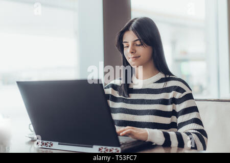 Cropped shot view of young woman keyboarding on laptop computer with blank copy space screen while sitting in cafe, blonde female student working on n Stock Photo