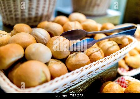 Close up of freshly baked, warm and tasty traditional bread buns in a basket with serving tongs on a luxury breakfast buffet. Stock Photo