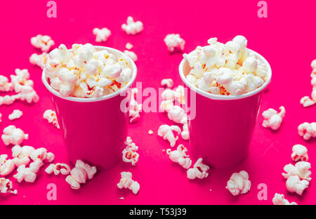Fresh salty pop corn in two bright pink carton containers, red color background, closeup view Stock Photo