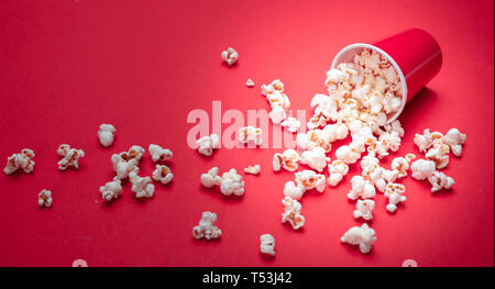 Fresh salty pop corn spilled out of a carton container, red color background, close up view Stock Photo