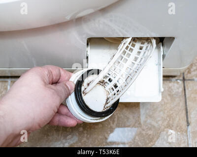 opening of the filter of old washing machine and water puddle on ceramic floor Stock Photo