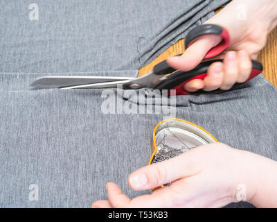 dressmaker cuts gray fabric with scissors close up on cutting table Stock Photo