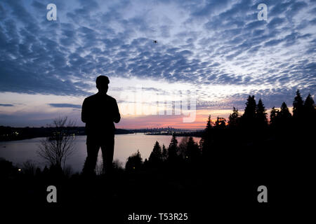 Silhouette of a man controlling a drone that is in the background Stock Photo
