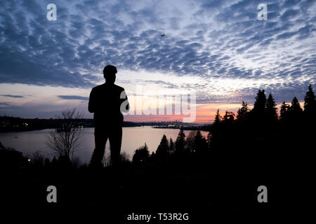 Silhouette of a man controlling a drone that is in the background Stock Photo