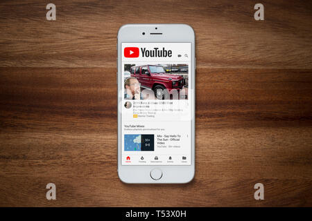 An iPhone showing the YouTube website rests on a plain wooden table (Editorial use only). Stock Photo