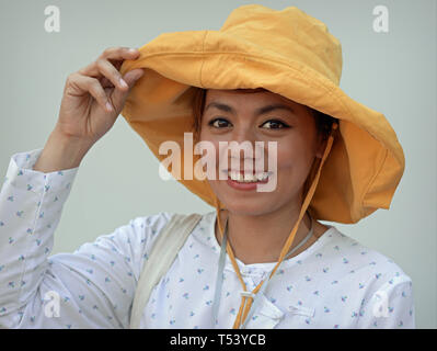 Young Thai woman with beautiful eyes wears a modern floppy hat and smiles for the camera. Stock Photo