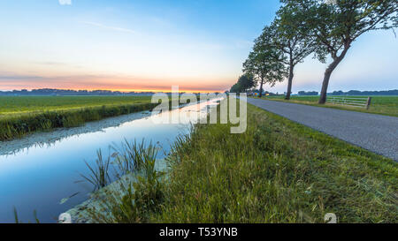 Netherlands open polder landscape with canal and road in open grassland countryside at sunset Stock Photo