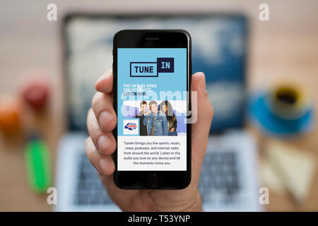 A man looks at his iPhone which displays the Tune In logo (Editorial use only). Stock Photo