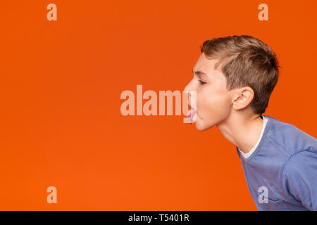 Little boy teasing someone, showing tongue and making face at free space aside, orange background Stock Photo