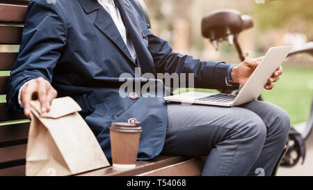 Lunch break. Businessman sitting outdoors with laptop and bicycle nearby, crop Stock Photo