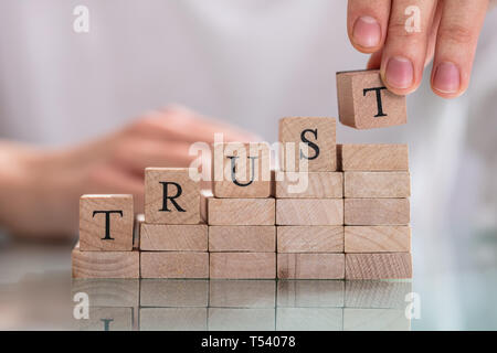 Woman's Hand Placing Last Alphabet Of Word Trust Over Wooden Block Stock Photo
