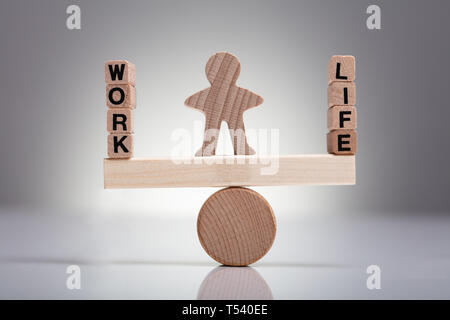 Human Figure Balancing Between Work And Life On Wooden Seesaw Against Gray Background Stock Photo