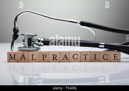 Stethoscope Over Malpractice Wooden Block On White Desk In Front Of Gray Background Stock Photo