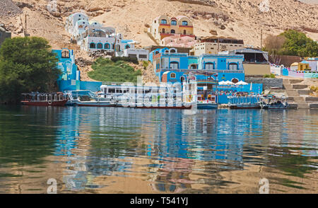 View from river Nile in Aswan Egypt to riverbank through rural countryside landscape with traditional Nubian village houses on shore and reflection Stock Photo