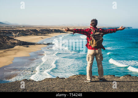 Alone happy traveler with backpack people man enjoying the destination place beach standing on a cliff and opening arms for success and joyful concept Stock Photo