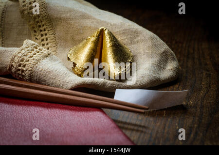 Lucky charm golden fortune cookie with chopsticks and dark moody lighting concept Stock Photo