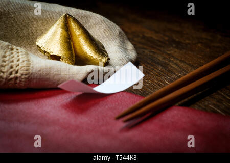 Lucky charm golden fortune cookie with chopsticks and dark moody lighting concept Stock Photo