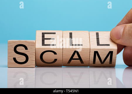 Man's Hand Holding Wooden Block With Sell And Scam Text Over Reflecting Desk Stock Photo