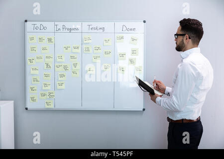 Side View Of Businessman Writing On Sticky Notes Attached To White Board In Office Stock Photo