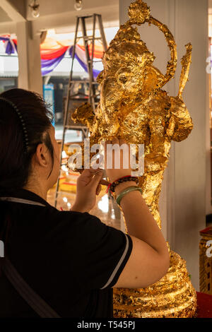 Thailand, Bangkok, Lak Muuang, City Pillar Shrine, worshipper applying gold leaf to Ganesh Hindu deity figure in main vihara prayer Hall Stock Photo