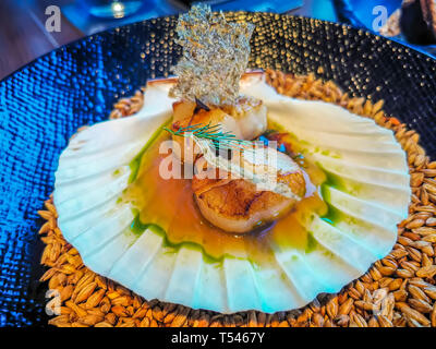 Pan seared Hokkaido scallops with wheat beer dashi, seaweed and malt chips served on a beautiful blue bowl Stock Photo