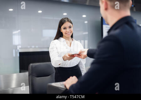 Friendly woman staff taking passport from passenger at airport check in desk Stock Photo