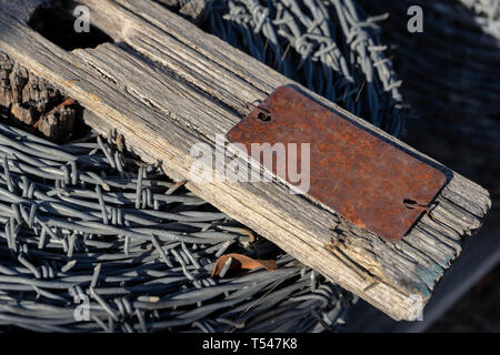 Roll of barbed wire on an old piece of wood with a rusted metal tag Stock Photo