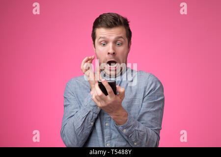 young man standing, using smartphone and watching video with amazed face. Stock Photo