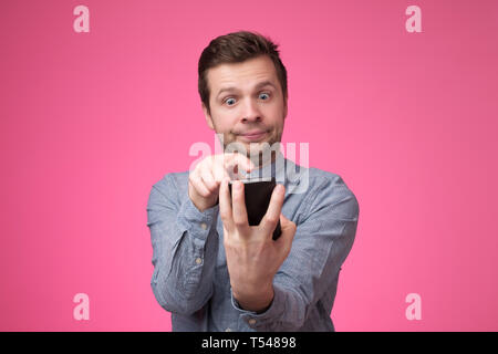 young man standing, using smartphone and watching video with amazed face. Stock Photo