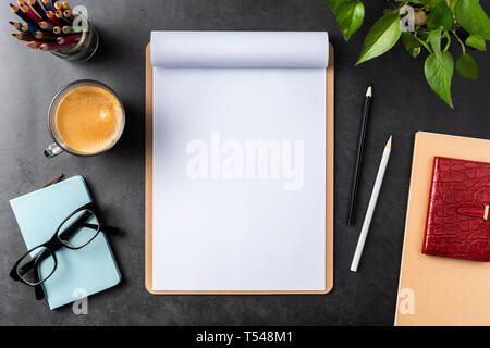 Design concept - top view of white A4 flipped paper with brown clipboard, potted plant, glasses, coffee, pencil on black background for mockup. real p Stock Photo