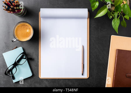 Design concept - top view of white A4 flipped paper with brown clipboard, potted plant, glasses, coffee, pencil on black background for mockup. real p Stock Photo