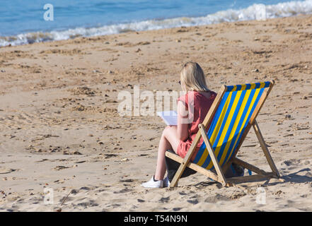 Bournemouth, Dorset, UK. 21st Apr 2019. UK weather: the heatwave continues with hot and sunny weather, as beachgoers head to the seaside to enjoy the heat and sunshine at Bournemouth beaches for the Easter holidays - mid morning and already beaches are getting packed, as sunseekers get there early to get their space. Woman sitting in deckchair reading book. Credit: Carolyn Jenkins/Alamy Live News Stock Photo