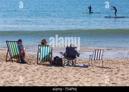 Bournemouth, Dorset, UK. 21st Apr 2019. UK weather: the heatwave continues with hot and sunny weather, as beachgoers head to the seaside to enjoy the heat and sunshine at Bournemouth beaches for the Easter holidays - mid morning and already beaches are getting packed, as sunseekers get there early to get their space. People sitting in deckchairs and chairs at the seashore while paddleboarders go by. Credit: Carolyn Jenkins/Alamy Live News Stock Photo