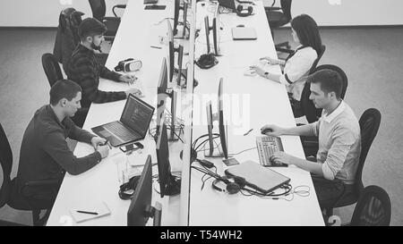 Young professionals working in modern office. Group of developers or programmers sitting at desks focused on desktops and laptops in IT company open s Stock Photo