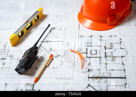 Orange hard hat, level meter, glasses and walkie talkie with blueprints on a table. Architectural and construction concept Stock Photo